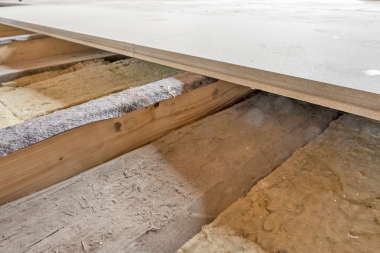 Erst klebten die Handwerker Auflaged?mmstreifen auf die seitlich an den Holzbalken angeschraubten und nivellierten Holzbohlen und verlegten darauf dann schwimmend die Bodenelemente