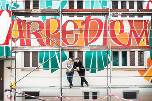  Etwa 15 x 9 m misst die Fassadenfläche, die von Andrea Wunderlich (rechts) nach ihrem eigenen künstlerischen Entwurf kalligrafisch gestaltet wurde. Links: Malermeisterin Beate Ripka vom Caparol FarbDesignStudio 