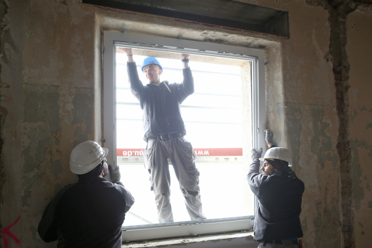 Mit vereinten Kräften werden die großen Fensterrahmen in die offene Laibung eingesetzt