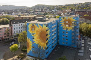  An der Hausfassade eines Hochhauses in Wuppertal blühen überdimensionale Sonnenblumen auf blauem Grund   