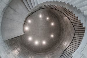  Die skulpturale Wendeltreppe schraubt sich durch die Sichtbetondecke von der erste in die zweite Etage der Ausstellung hinein 