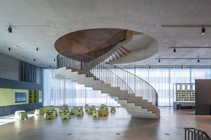  Die skulpturale Wendeltreppe schraubt sich durch die Sichtbetondecke von der erste in die zweite Etage der Ausstellung hinein 