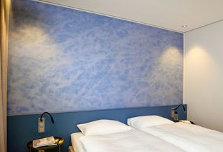 In wolkigem Blau individuell gestaltete Fläche einer Kopfwand in einem der Gästezimmer im B-Wohnen von Brillux in Münster