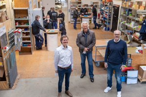  Hermann-J. Kreitmeir (Mitte) mit den Geschäftsführern Thomas Klarmann (links) und Marc Böckmann (rechts) in ihrem SHK-Betrieb in Neuenkirchen-Vörden. Im Hintergrund sind die Mitarbeiter beim werktäglichen „Feierabend-Feedback-Gespräch.“  