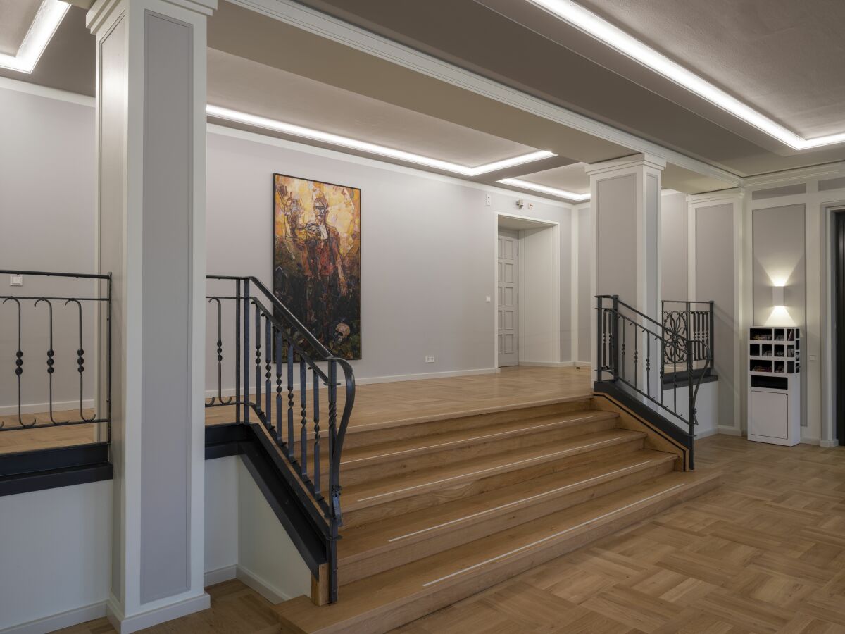 Die Wandflächen in den Foyers wurden mit „Sensocryl ELF 267“ in Mittelgrau gestrichen; davon abgesetzt sind hellere Bereiche an Säulen, Kassettenumrandungen und den die Türen einfassenden Stuckelementen