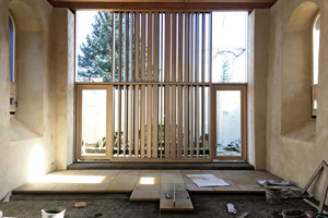  Den sehr modernen Abschluss des Innenraums bildet eine raumhohe, verglaste Pfosten-Riegel-Fassade mit unterschiedlich dicht gesetzten, vertikalen Holzlamellen 