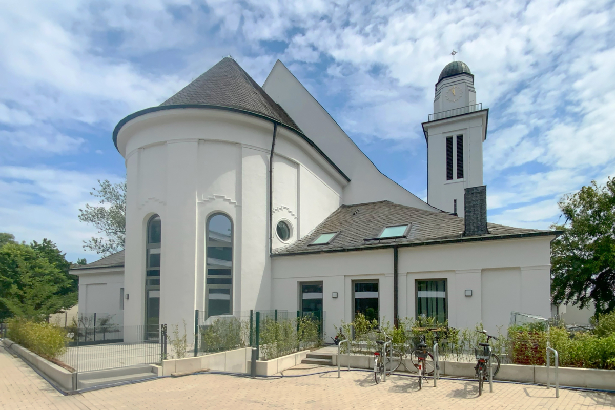 Die ehemalige Kirche ist mit verschiedenen Fensterformen in Betongrau ausgestattet ? darunter Bauelemente mit aufge-koppeltem Rundbogenfenster, Pfosten-Riegel-Konstruktionen sowie ein Rundfenster