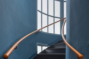  Treppenhaus mit blauen Wänden, orange farbenem Handlauf und dunklem Belag 