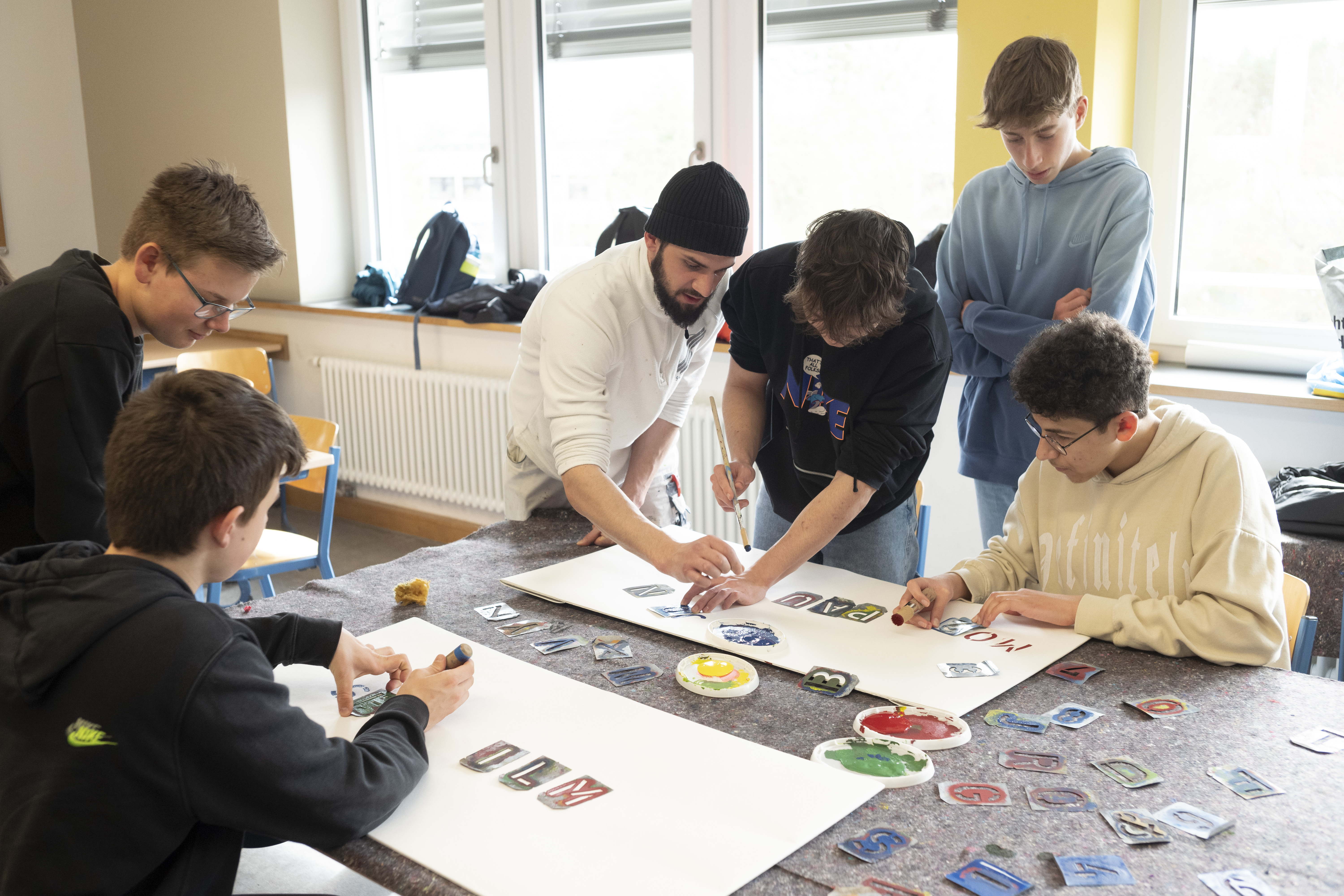 Auf Tuchfühlung mit dem Handwerk: Mitarbeiter Deniz Celdik (Mitte) vom Malerfachbetrieb Scholten GmbH gibt Schülerinnen und Schülern des Albert-Schweizer-Gymnasiums Erlangen Einblicke in seinen Berufsalltag