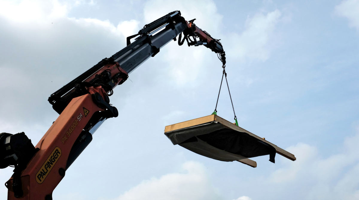 Ein vorgefertigtes Fassadenelement mit Strohdämmung hängt am Kran