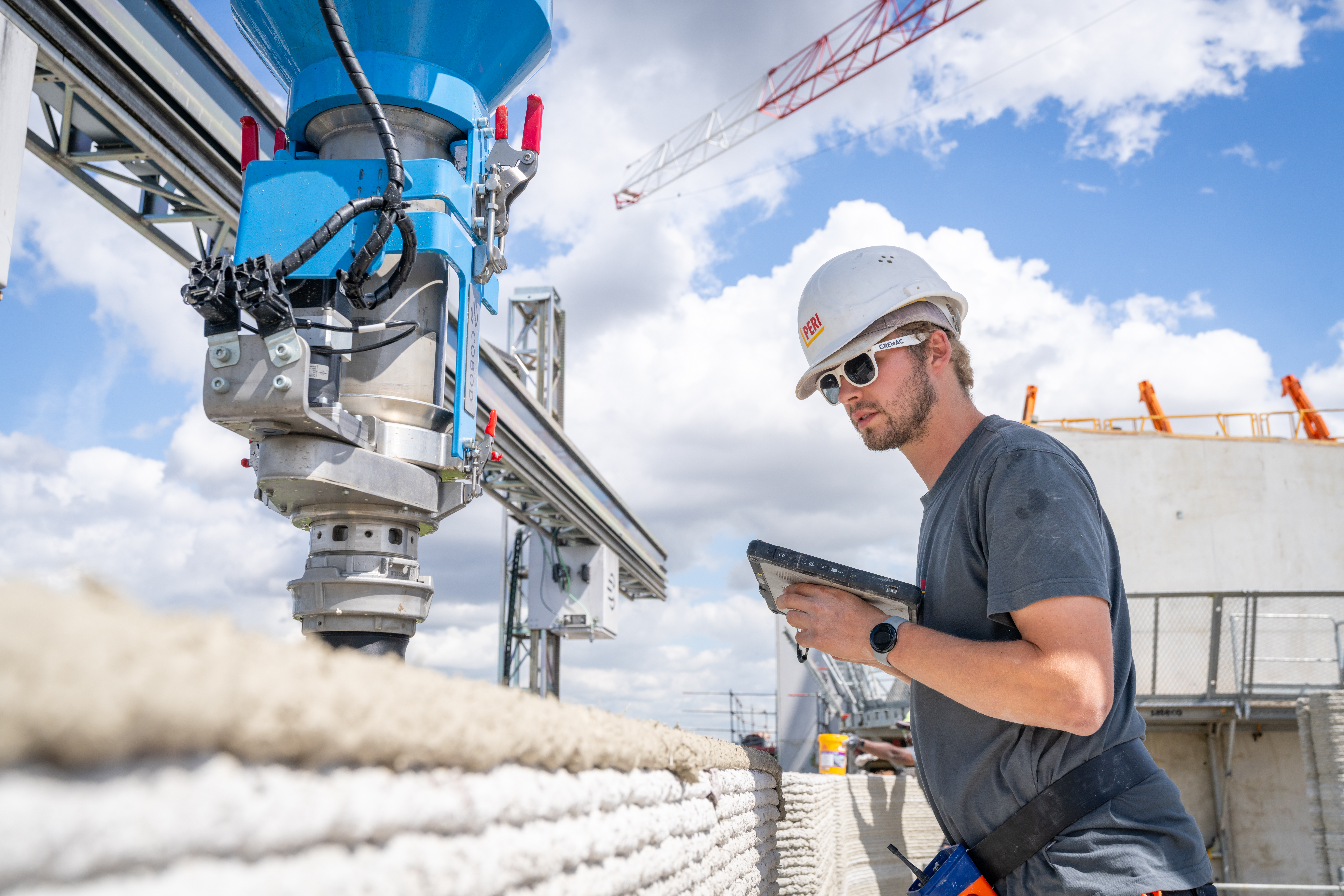 Durch schichtweises Extrudieren von Beton werden die tragenden Außen- und Innenwände erzeugt. Die Bediener arbeiten ergonomisch und steuern den Prozess per Tablet