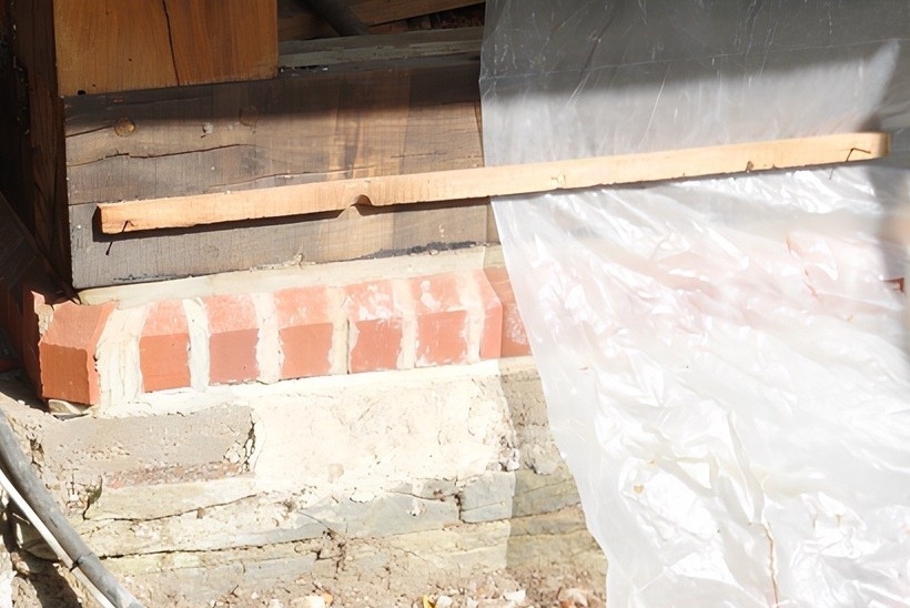 Auf dem Natursteinsockel sitzt jetzt eine Lage vorne abgeschrägter Vollziegel, gefolgt von einer Bitumen-Horizontalsperre und neuen Schwellhölzern aus Eiche