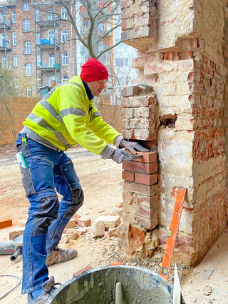 Die gerumpelten neuen Ziegel passt der Handwerker in die Bestandsfassade ein