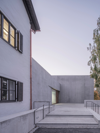 Die bauliche Erweiterung aus Infraleichtbeton schließt bündig an den Altbau an. Links scheint sich die Verglasung des Eingangs in den Beton zu schieben