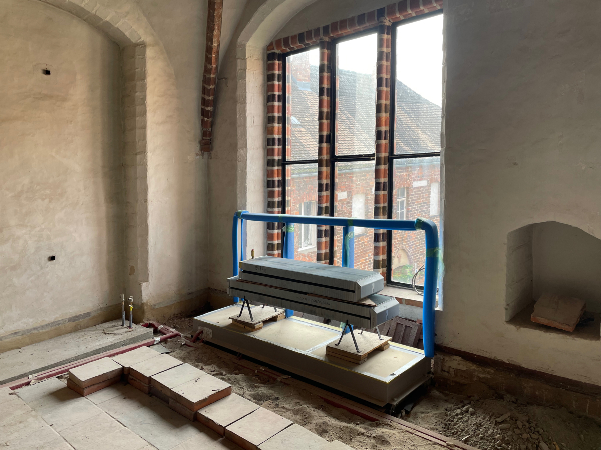 Die unverkleideten Konvektoren stehen am Ende vor der Wand. Der noch blau verpackte Anprallschutz schützt die Fenster ohne Sicherheitsglas