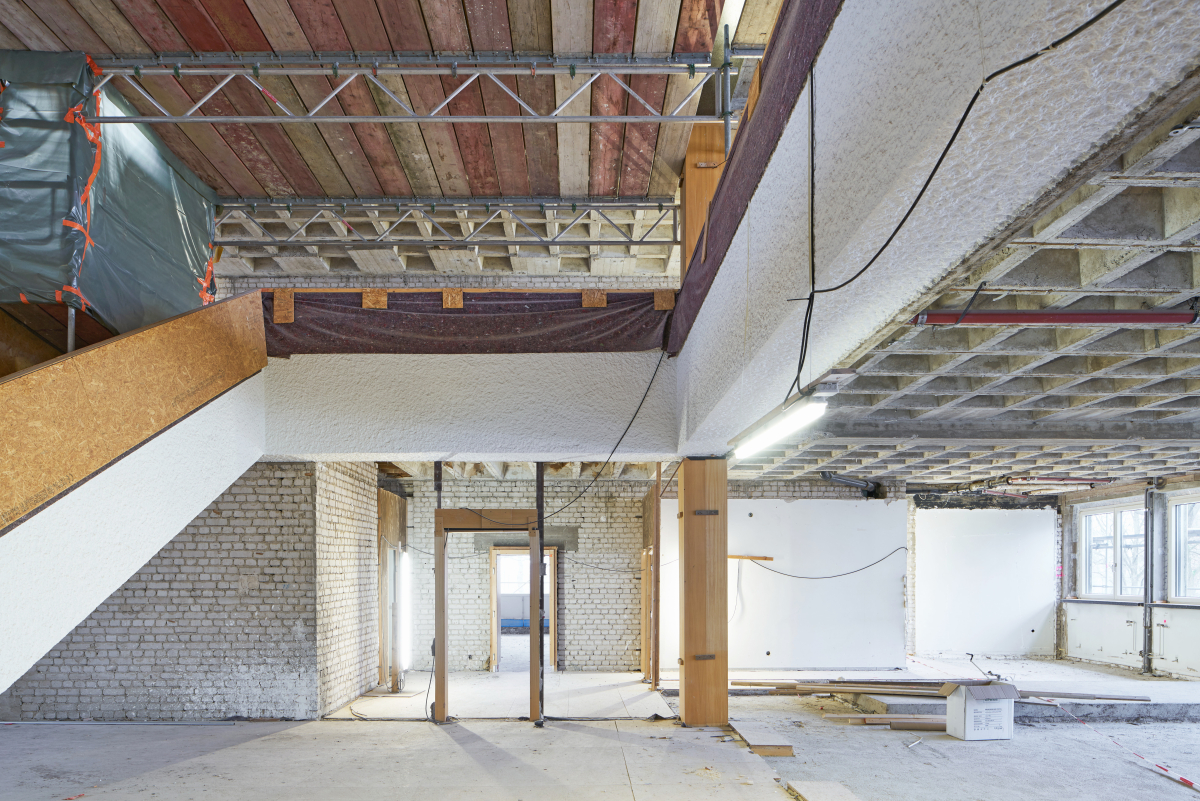 Im Atrium führt die einläufige Treppe auf die umlaufende Galerie im ersten Obergeschoss. Die Betonwerksteinplatten der Stützen wurden während der Bauphase geschützt