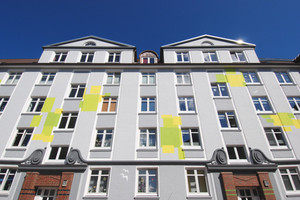  Die straßenseitige Fassade des Wohnblocks zeigt sich in edlen Grautönen, die die Schmuckelemente betonen und fröhlich-aufglockerten Farbflächen 
