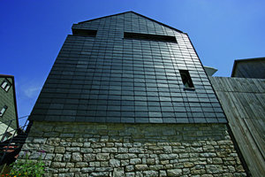  Bei der Wahl der Materialien vermischte der Architekt Tradition und Moderne: Der alte Sandsteinsockel und die sägeraue Verbretterung der Wand vorm Innenhof stehen im Kontrast zur modernen Schieferfassade in Kreuzfugenoptik 