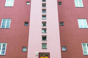  Ein vorspringendes, in hellem Rot gefasstes Treppenhaus mit einem vertikalen Band kleiner quadratischer Fenster 