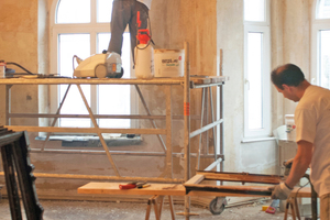  Während die Stuckatur an der Decke freigelegt wird, arbeitet ein Kollege an einem historischen Fenster 